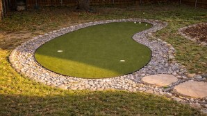 Un parcours de mini-golf doté d’un green, bordé de petits cailloux, et agrémenté d’une clôture en bois en arrière-plan.
