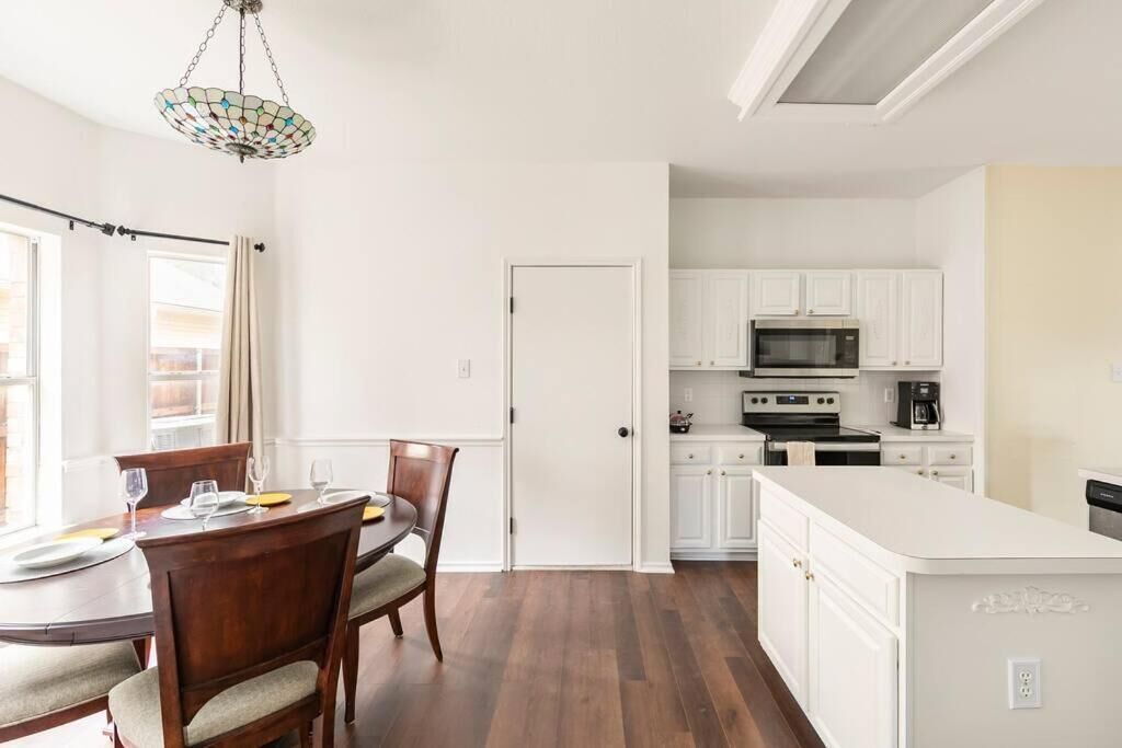 A modern kitchen with white cabinets, a central island, and a dining area with a round table and chairs.
