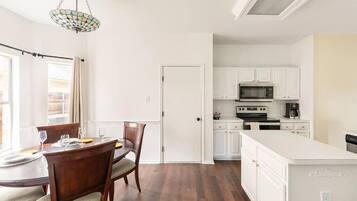A modern kitchen with white cabinets, a central island, and a dining area with a round table and chairs.