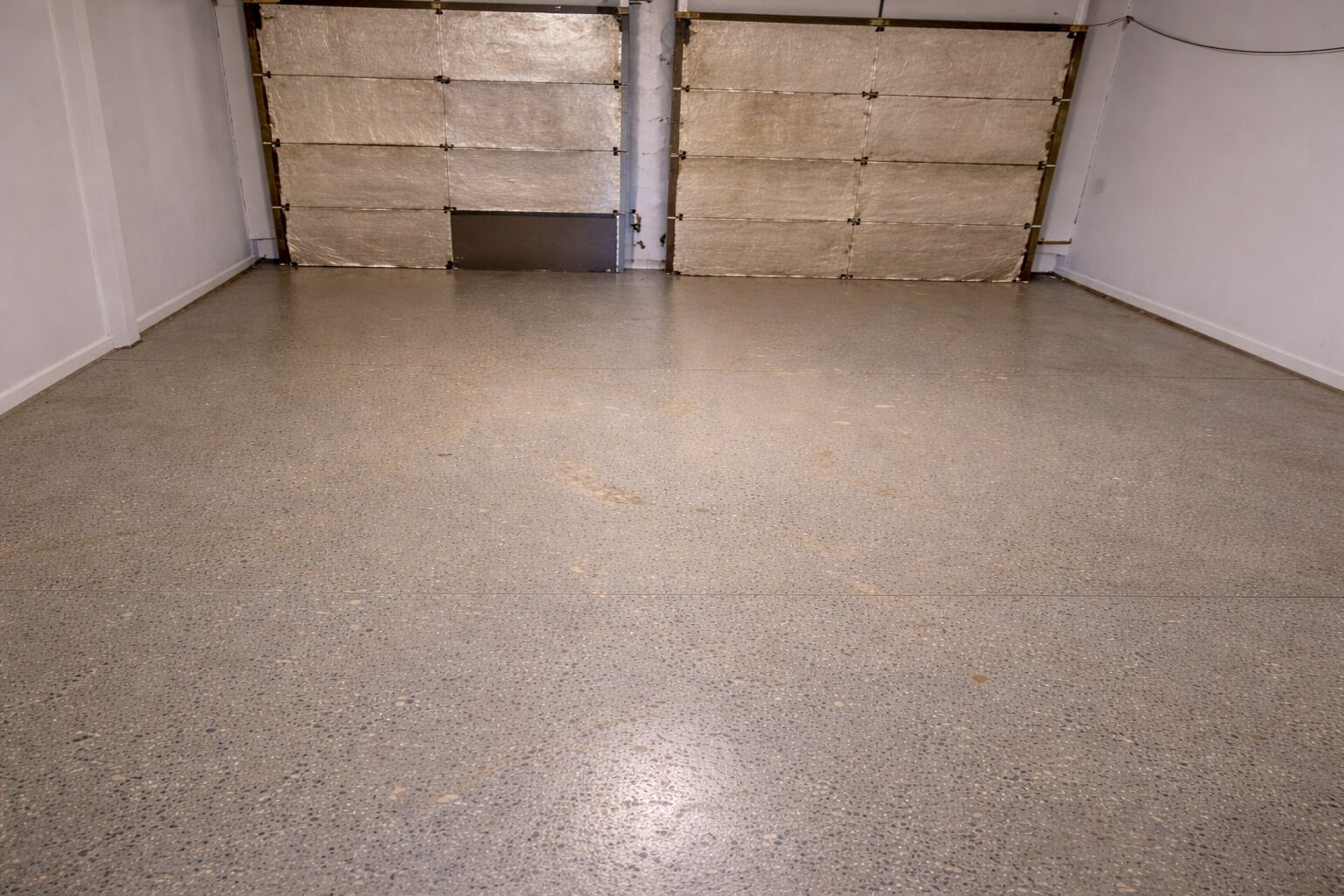 Una habitación con piso de concreto y dos puertas grandes cerradas.