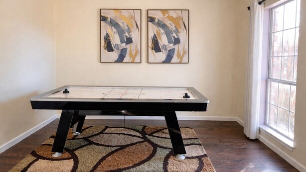 Une pièce avec une table de billard, deux tableaux abstraits accrochés au mur et une grande fenêtre avec des rideaux.