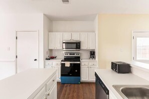A modern kitchen with white cabinets, a black and blue oven, a microwave, a toaster, and a dishwasher. - Spacious home with putting green and game room (Carrollton)