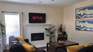 Un salon avec une cheminée, un canapé, une table basse et un téléviseur affichant le logo « NETFLIX ».