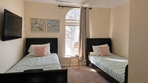 Une chambre avec deux lits, une fenêtre avec des rideaux et des œuvres d’art murales.