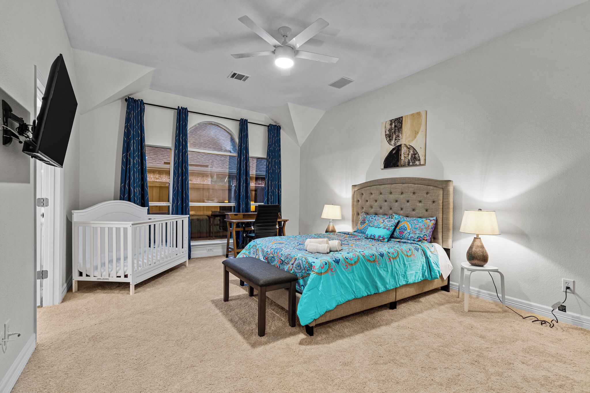 Ein Schlafzimmer mit einem Bett, einem Babybett, einem Schreibtisch und einem Stuhl.