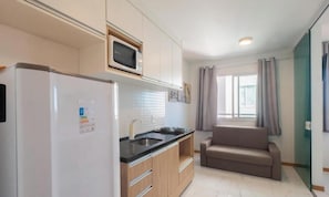 A compact kitchen with a refrigerator, microwave, and a sink. There is a sofa in the adjacent living area. - Apt. in Condo. w/ sea View and gym Sip0206 (Salvador)