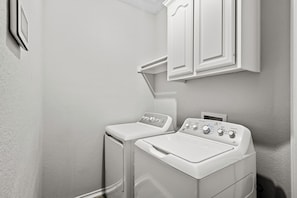 A laundry room with two white washing machines and a cabinet above them. - Spacious 4-Bedroom Home for Relocating Families (Fort Worth)