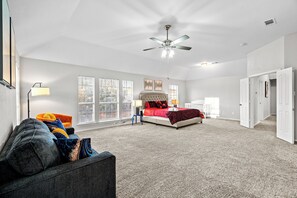 A spacious bedroom with a large bed, a ceiling fan, and a view through the windows. - Spacious 4-Bedroom Home for Relocating Families (Fort Worth)