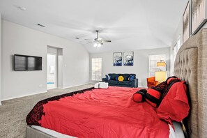 Ein Schlafzimmer mit einem großen Bett, einem Deckenventilator, einem an der Wand montierten Fernseher und einem Fenster mit Jalousien.