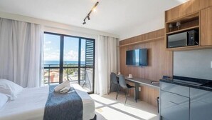 Een hotelkamer met een bed, een bureau, een televisie en uitzicht op zee.