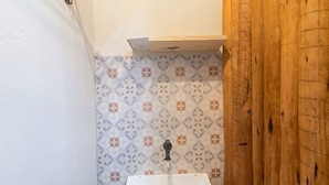 A bathroom with a white sink, patterned tiles, and a wooden door. - Studio w/ Balcony in Arraial D'ajuda Ipe0001 (Porto Seguro)