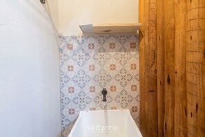 A bathroom with a white sink, patterned tiles, and a wooden door. - Studio w/ Balcony in Arraial D'ajuda Ipe0001 (Porto Seguro)