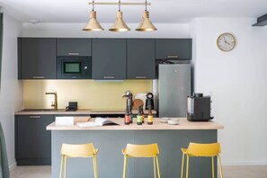 A modern kitchen with dark cabinets, a central island, yellow chairs, and a clock on the wall.
