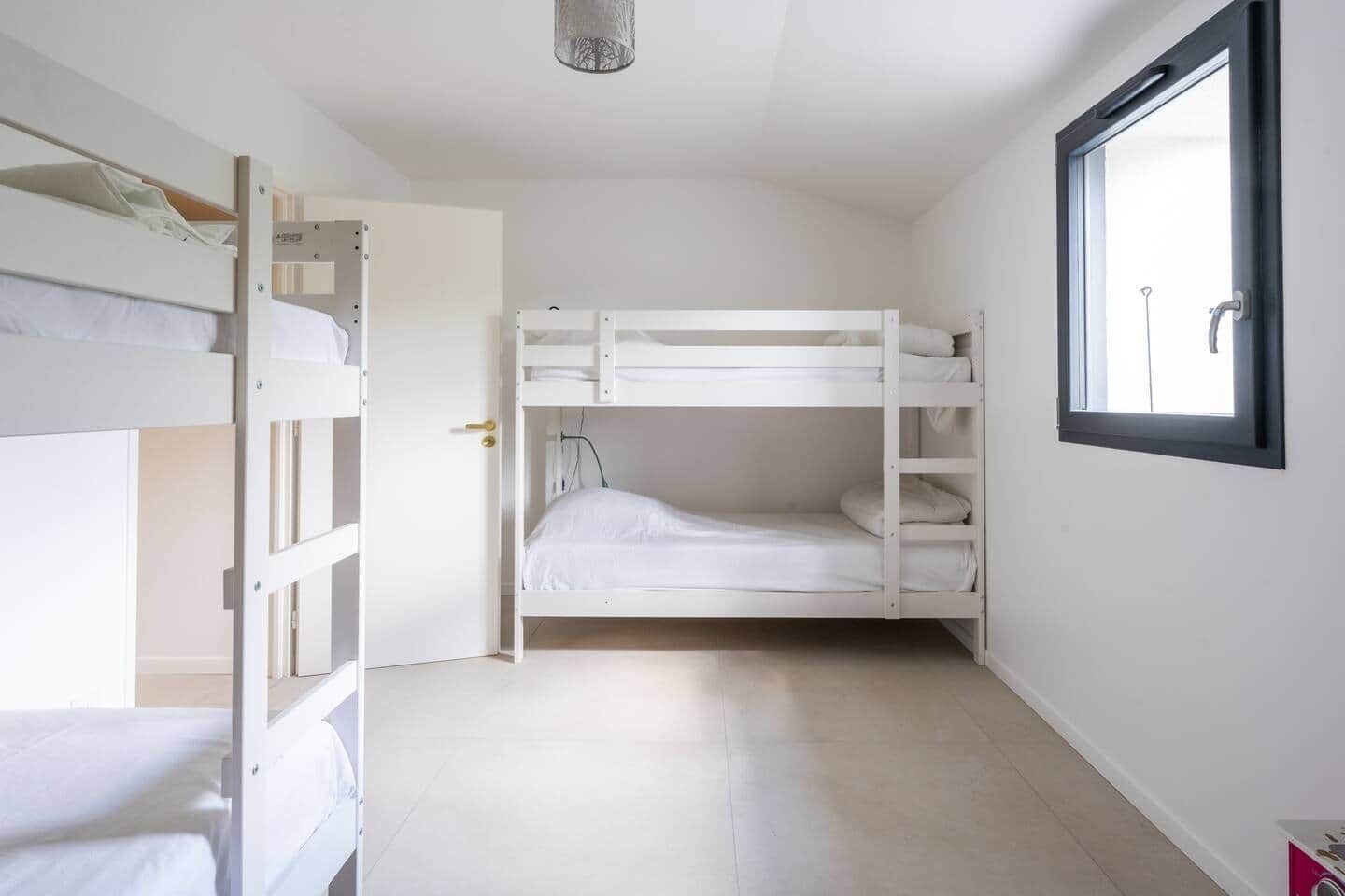 Ein Zimmer mit Etagenbetten, einer Tür, einem Fenster und einer Lampe.