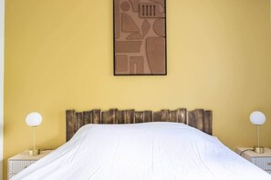 A bed with a white sheet, a wooden headboard, and a wall-mounted abstract art piece.