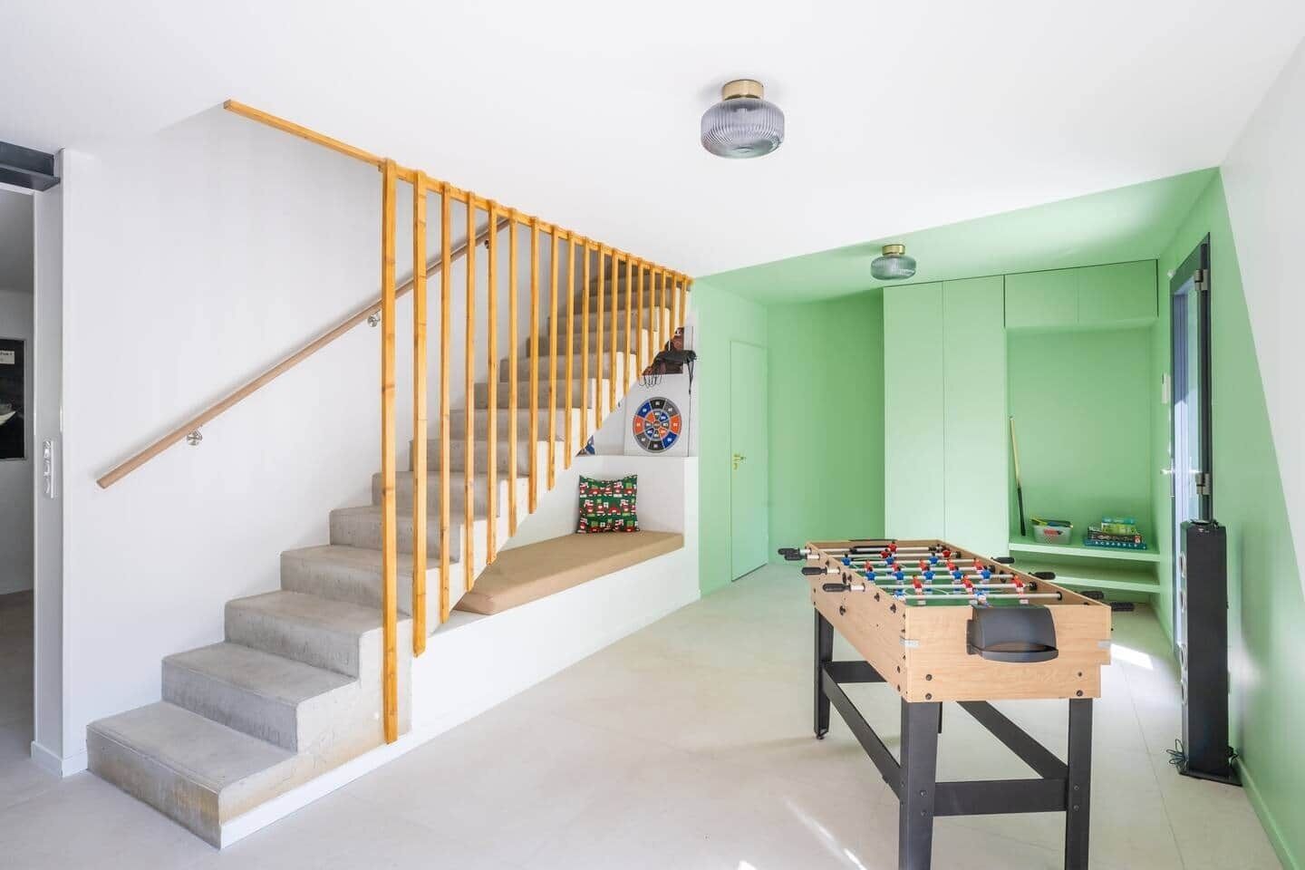 A modern interior with a staircase, a foosball table, and a dartboard.