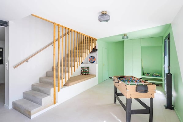 A modern interior with a staircase, a foosball table, and a dartboard.