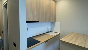 Una cocina compacta con gabinetes blancos, encimera de madera y luces empotradas en el techo.