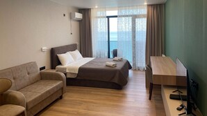 Habitación de hotel con cama, escritorio, silla, sofá y vistas al exterior.