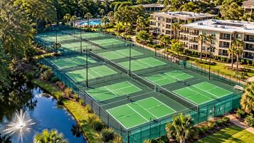 A tennis court complex surrounded by greenery and a body of water.
