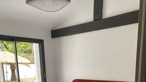 Ein Schlafzimmer mit einem großen Bett, einem Nachttisch, einer Lampe und einem Fenster mit Blick auf Palmen.