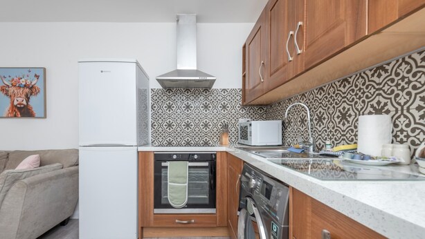 A compact kitchen with a refrigerator, oven, microwave, and dishwasher. - Modern 2-bed Flat Near Hackney Central (London)