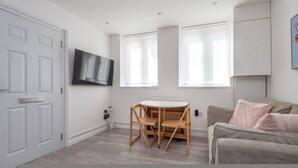 A modern living room with a sofa, a TV, a dining table with chairs, and large windows. - Modern 2-bed Flat Near Hackney Central (London)