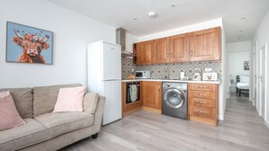 A compact kitchen with wooden cabinets, a washing machine, and a refrigerator. - Modern 2-bed Flat Near Hackney Central (London)