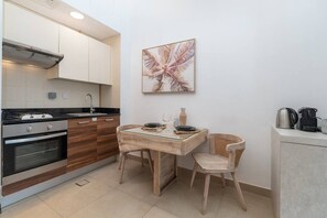 A compact kitchen with a dining area, featuring a stove, oven, sink, and a table with chairs. - Marina Escape Steps from JBR Beach (Dubai)