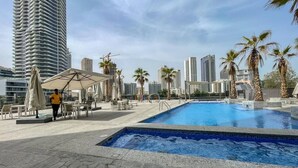 A rooftop pool area with lounge chairs and umbrellas, surrounded by palm trees and high-rise buildings. - Marina Escape Steps from JBR Beach (Dubai)