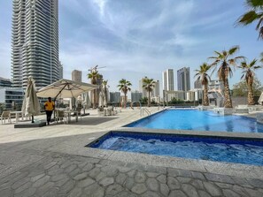 A rooftop pool area with lounge chairs and umbrellas, surrounded by palm trees and high-rise buildings. - Marina Escape Steps from JBR Beach (Dubai)