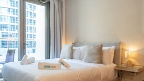A hotel room with a bed, pillows, a bedside table with a lamp, and a window with curtains. - Marina Escape Steps from JBR Beach (Dubai)