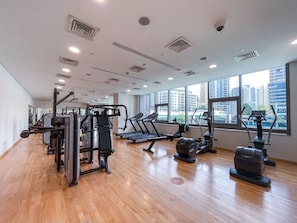 A gym with various exercise equipment, large windows, and a wooden floor. - Marina Escape Steps from JBR Beach (Dubai)