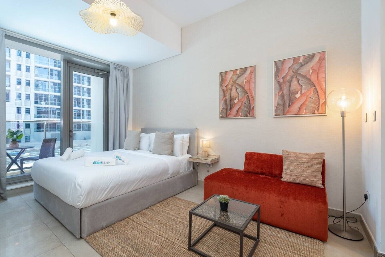 A hotel room with a bed, a red sofa, a small table, and artwork on the wall.