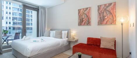 A hotel room with a bed, a red sofa, a small table, and artwork on the wall.