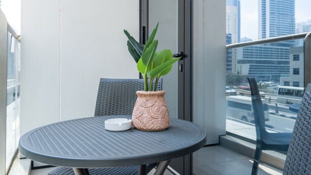 A balcony with a round table, a potted plant, and a chair. - Marina Escape Steps from JBR Beach (Dubai)