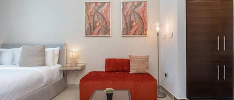 Une chambre à coucher moderne avec un lit, un canapé rouge, deux tableaux abstraits, une table de chevet et une armoire.
