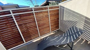 Ein Patio mit Holzzaun, einem Metallstuhl und einem Fliesenboden.