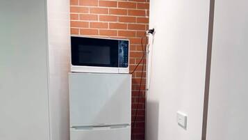 Een kleine keuken met een witte koelkast, een magnetron erboven en een bakstenen muur.