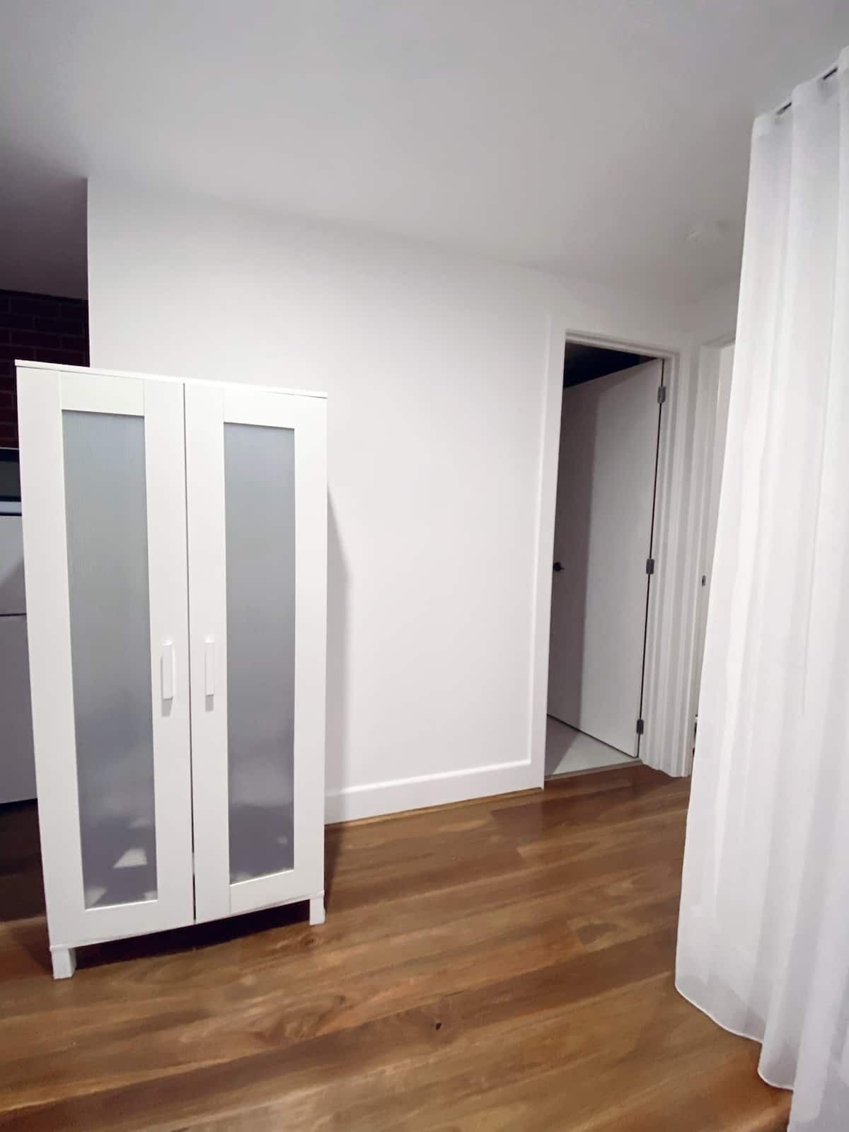 Een kamer met een houten vloer, witte muren en een witte garderobe met glazen deuren.