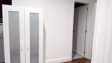 Een kamer met een houten vloer, witte muren en een witte garderobe met glazen deuren.