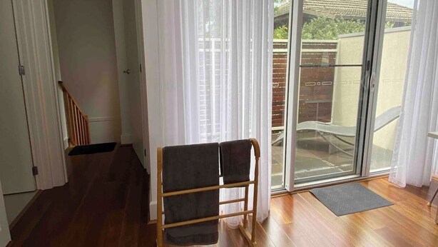 Ein Zimmer mit Holzboden, einer Bank, einer Schiebeglastür, die auf einen Balkon führt, und einer Treppe.