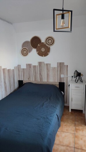 A bedroom with a bed, a bedside table, a lamp, and wall decor. - One-bedroom apartment, sleeps 4, in Cap d'Agde, ground floor with garden, pets allowed (Agde)