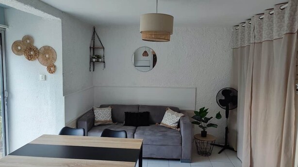Ein Wohnzimmer mit einer Couch, einem Esstisch, einem Deckenventilator und einer Topfpflanze.