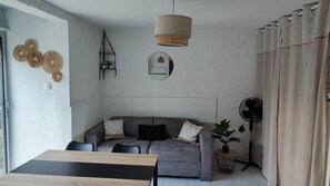 A living room with a sofa, a dining table, a ceiling fan, and a potted plant. - One-bedroom apartment, sleeps 4, in Cap d'Agde, ground floor with garden, pets allowed (Agde)