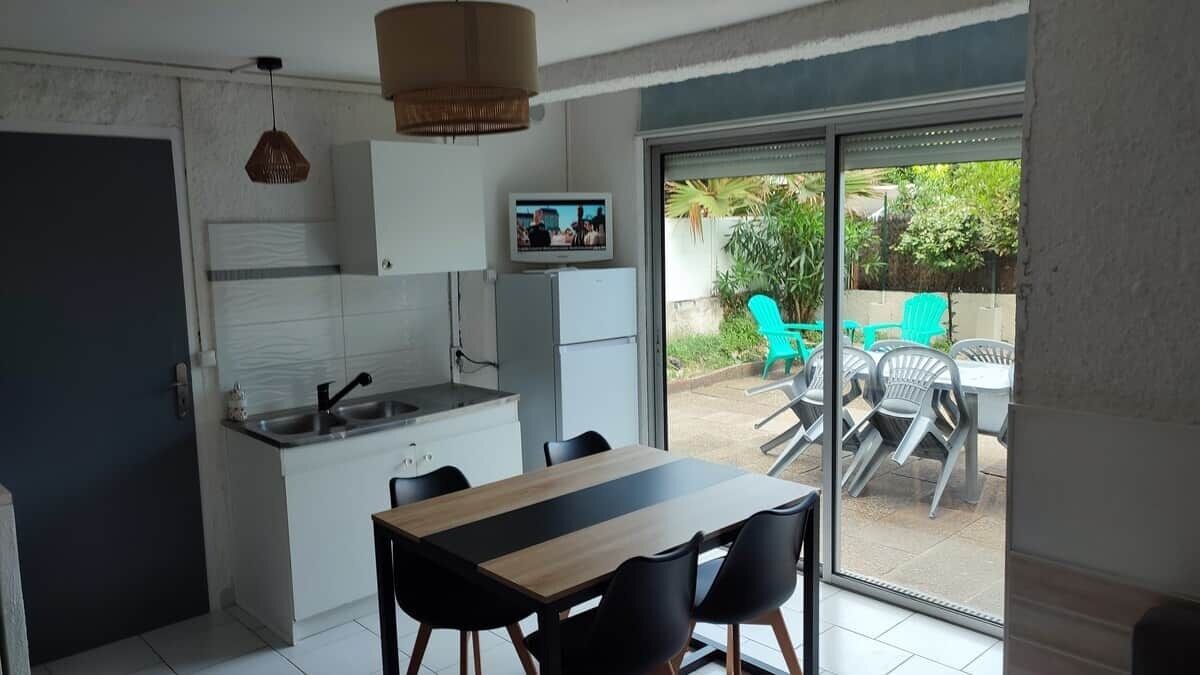 A compact kitchen with a dining area, a television, and a sliding glass door leading to an outdoor patio with chairs.