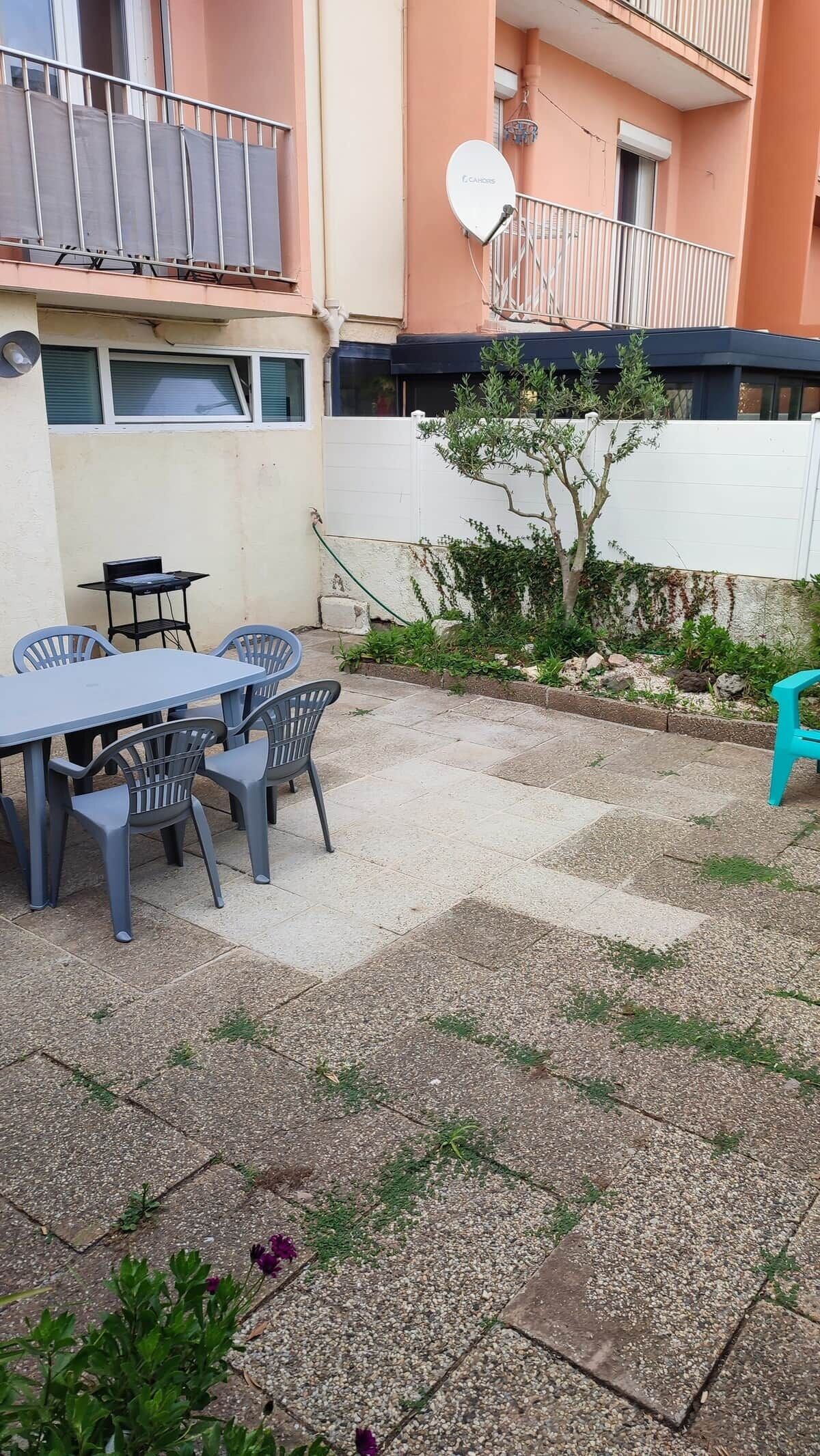 An outdoor patio area with a table and chairs, a small tree, and a white wall.