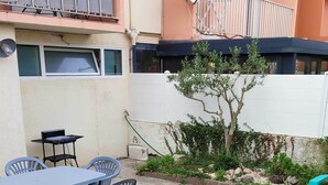 Ein Terrassenbereich im Freien mit Tisch, Stühlen, einem kleinen Baum und einer weißen Wand.