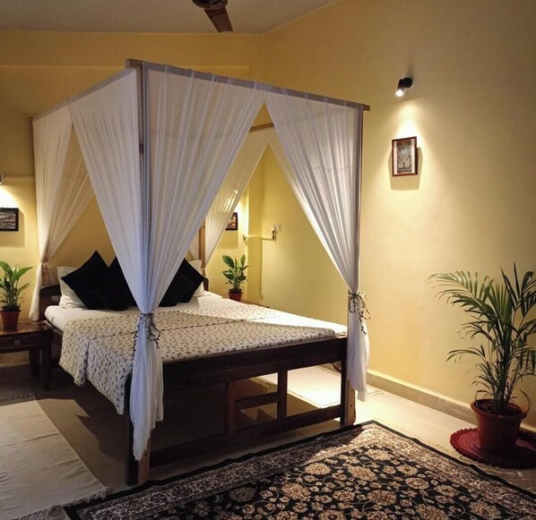 A four-poster canopy bed with a floral bedspread, a nightstand with a lamp, and a potted plant beside the bed. - Hill view apartment (Ashwem)