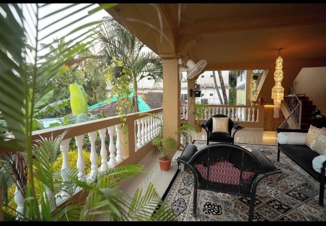 A covered outdoor seating area with a balcony, potted plants, and a staircase.